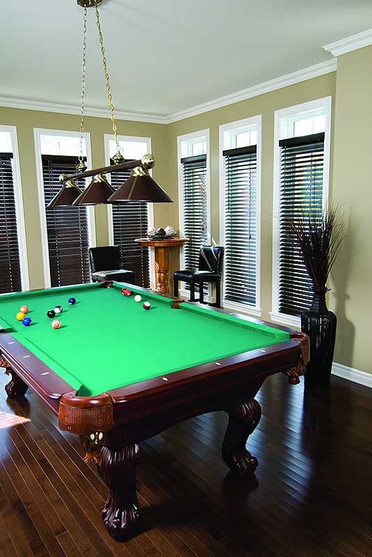 Interior game room with a pool table, chandelier, dark wood floor, and windows with blinds.