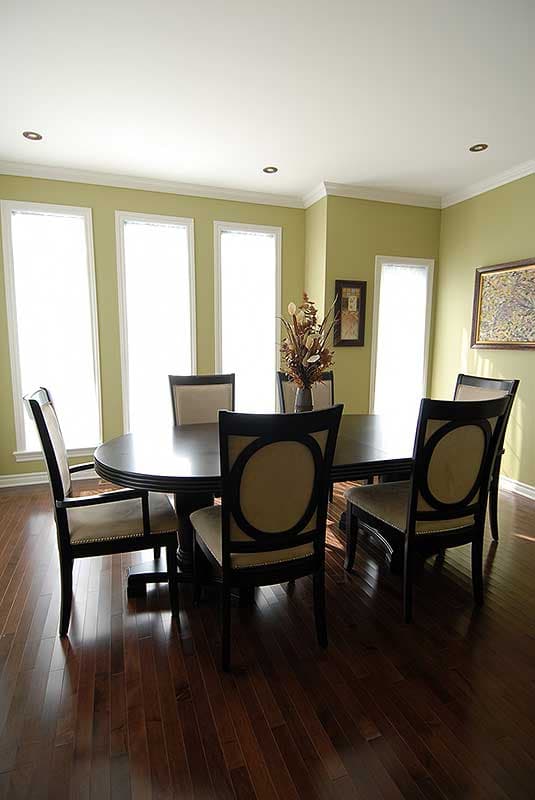 Dining room with oval table, six chairs with circular back details, and large windows. Hardwood floors.