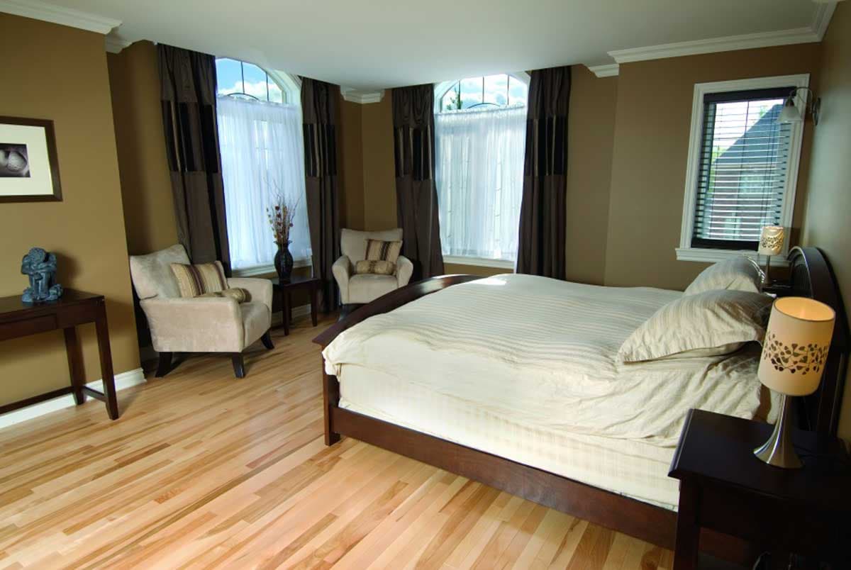 Bedroom with arched windows, two armchairs, and a wooden bed. Hardwood floors visible.