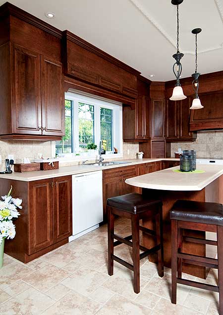 Kitchen with dark wood cabinets, white countertop, window over sink, island with bar stools, and pendant lighting.