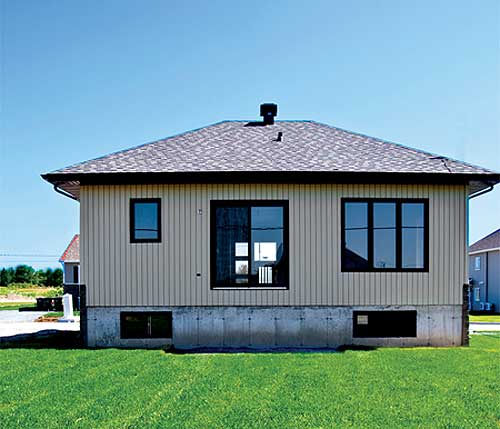 House plan exterior: one-story home with beige vertical siding, asphalt shingle roof, and a concrete foundation with basement windows.