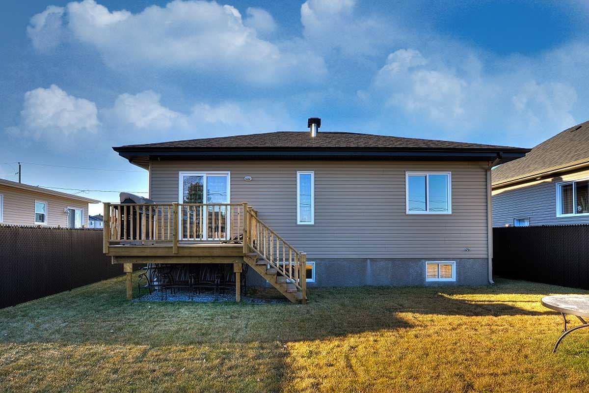 House plan exterior: Ranch style with tan siding, prominent wooden deck with stairs, and multiple windows.