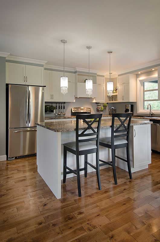 Kitchen interior with island, pendant lights, stainless steel refrigerator, and light wood flooring.