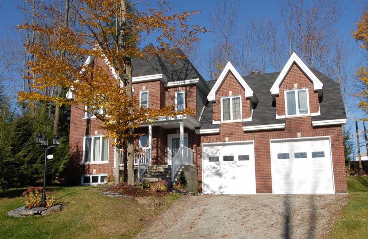Two-story brick house plan with covered porch, gabled dormers, and attached two-car garage.