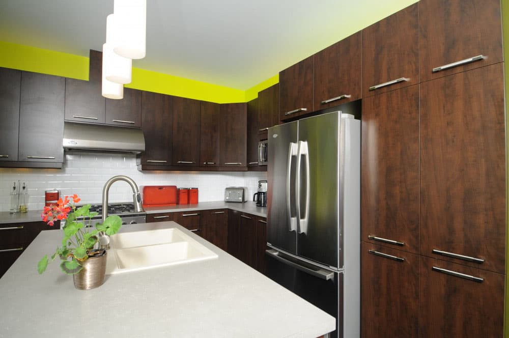 Modern kitchen with dark wood cabinets, stainless steel appliances, island with sink, and lime green accent wall.