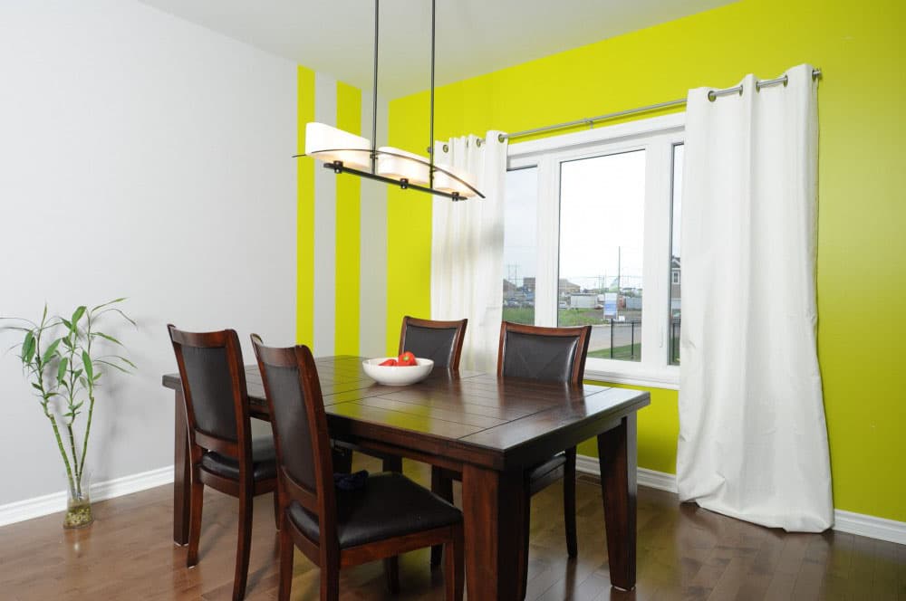 Dining room with dark wood table and chairs, contemporary light fixture, and lime green accent wall.