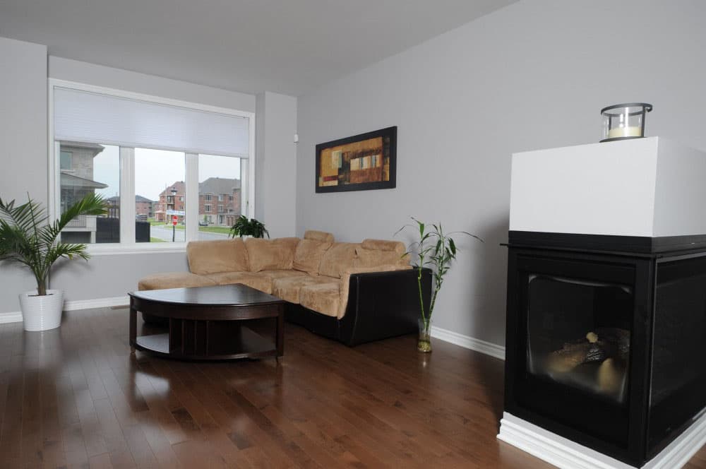 Living room with sectional sofa, gas fireplace, coffee table, and large window overlooking street.