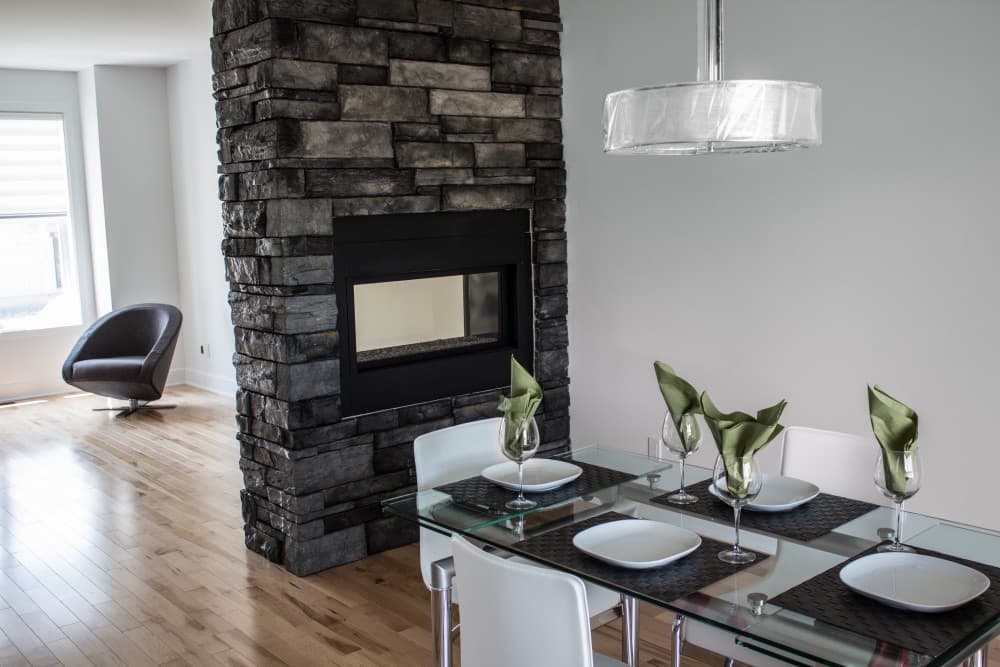 Interior rendering of a dining area featuring a stone-clad fireplace and a glass-top dining table.