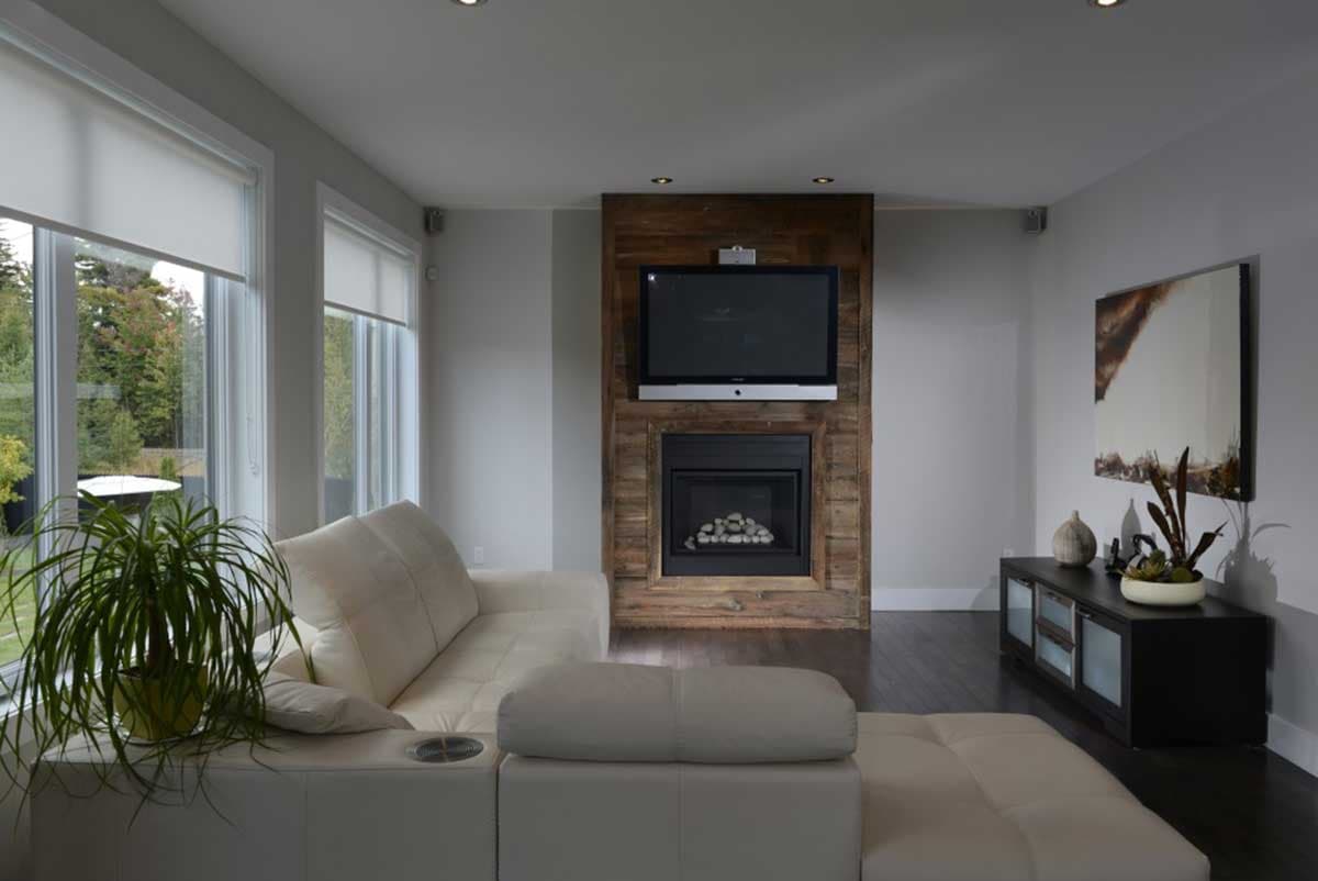 Living room with white sectional sofa, fireplace with wood surround, mounted television, and large windows.