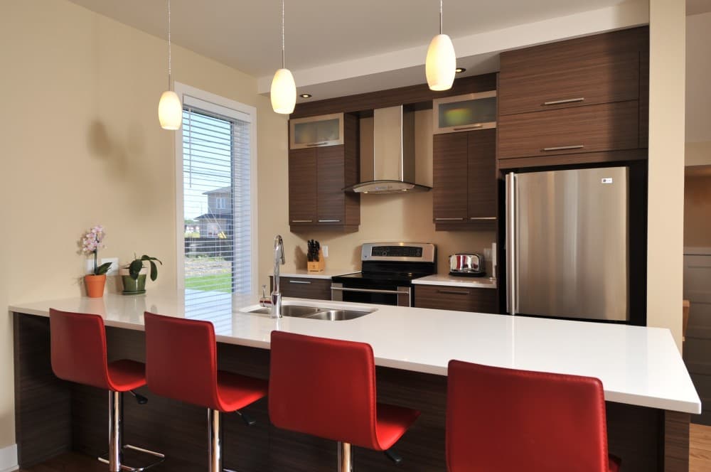 Modern kitchen with dark wood cabinets, stainless steel appliances, a white quartz island with red bar stools, and pendant lighting.