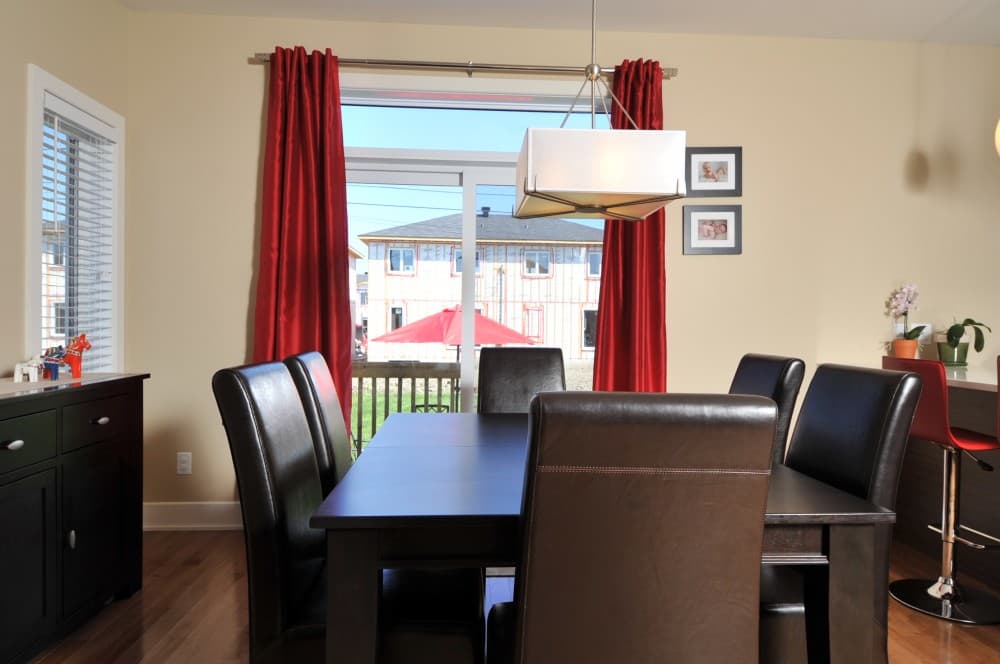 Dining room with dark table and chairs, looking through window at house construction with red umbrella.