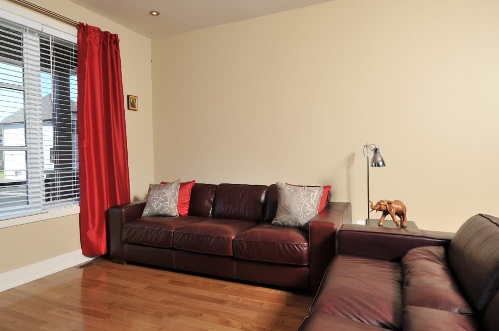 Interior view: Living room with leather sofa, decorative pillows, red curtains, and wood flooring.