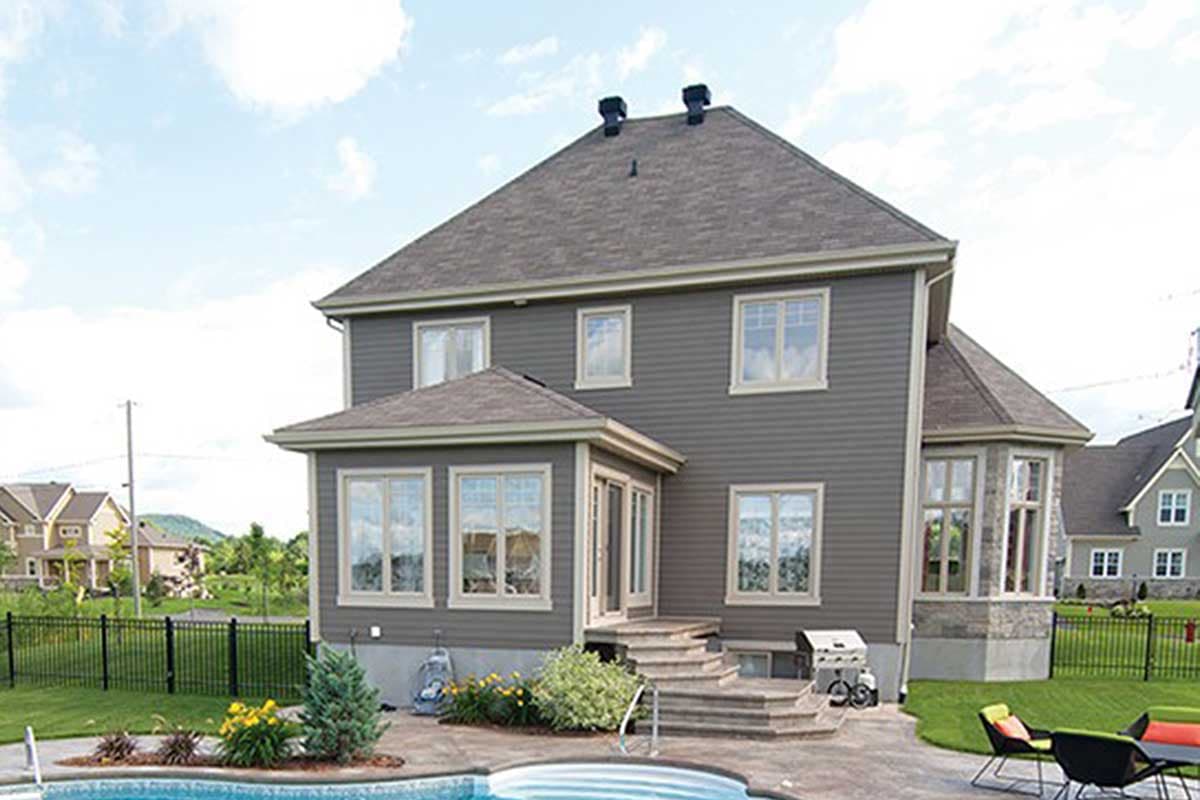 House plan exterior, two stories, gray siding, gable roof, bay window, and sunroom addition.