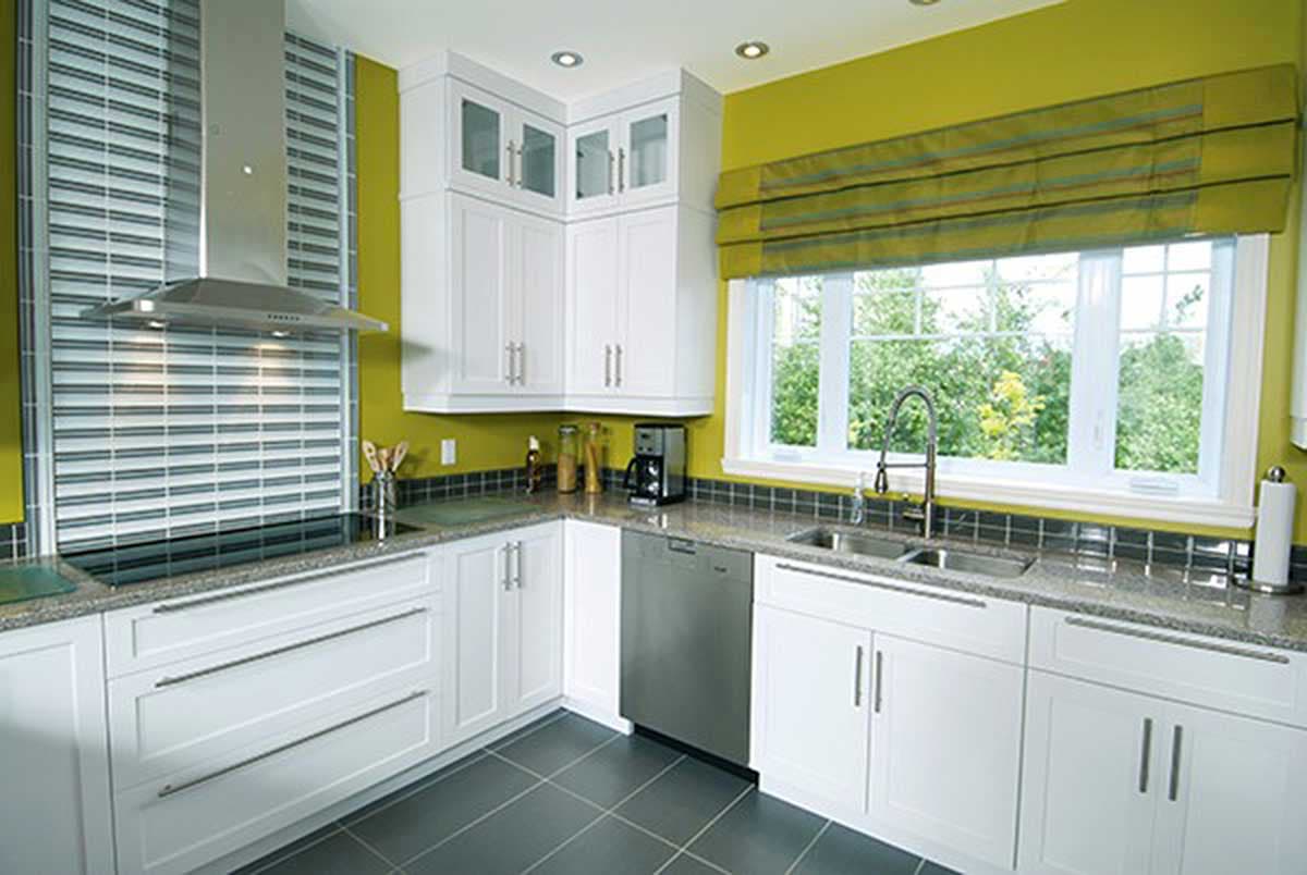 L-shaped kitchen interior with white cabinets, granite countertops, stainless steel appliances, and a large window.