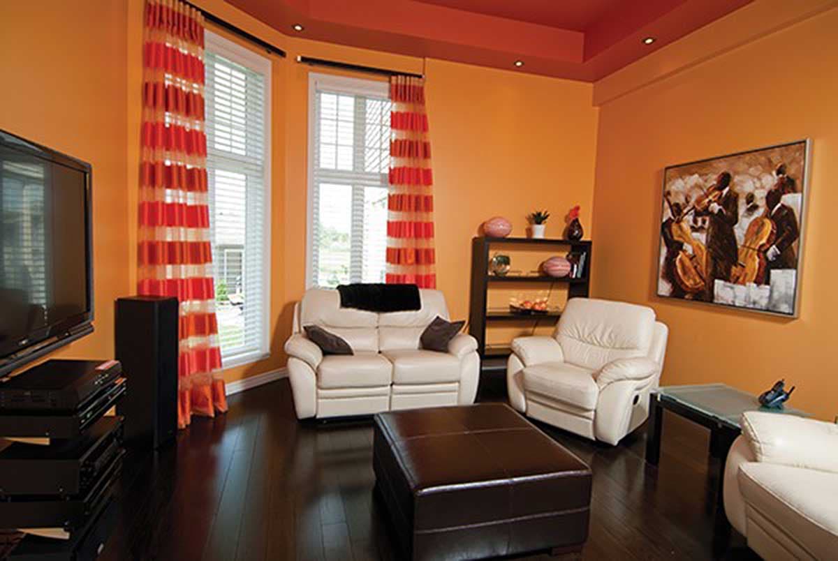 Living room with cream sofas, leather ottoman, dark wood floors, and orange walls with a recessed ceiling.