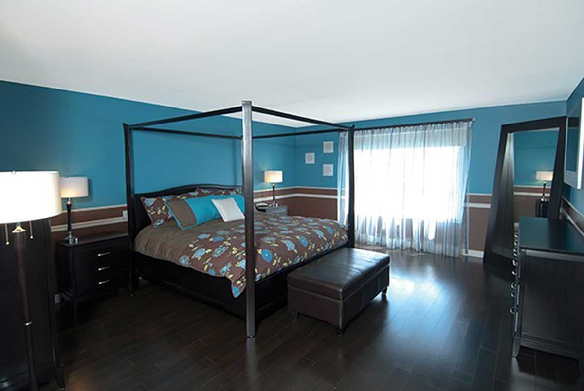 Primary bedroom with four-poster bed, dark wood furniture, and large window with sheer curtains.