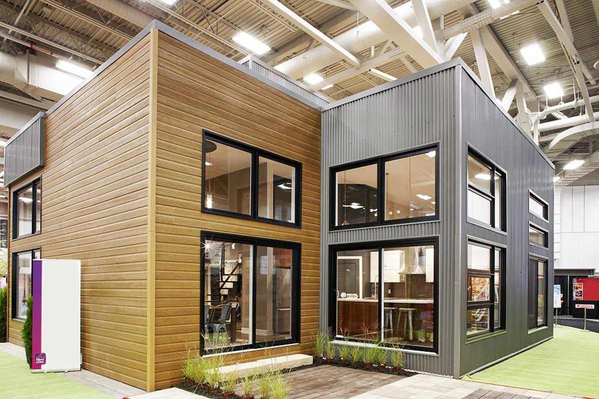 Modern house exterior with wood siding and corrugated metal cladding, featuring large black-framed windows and two stories.