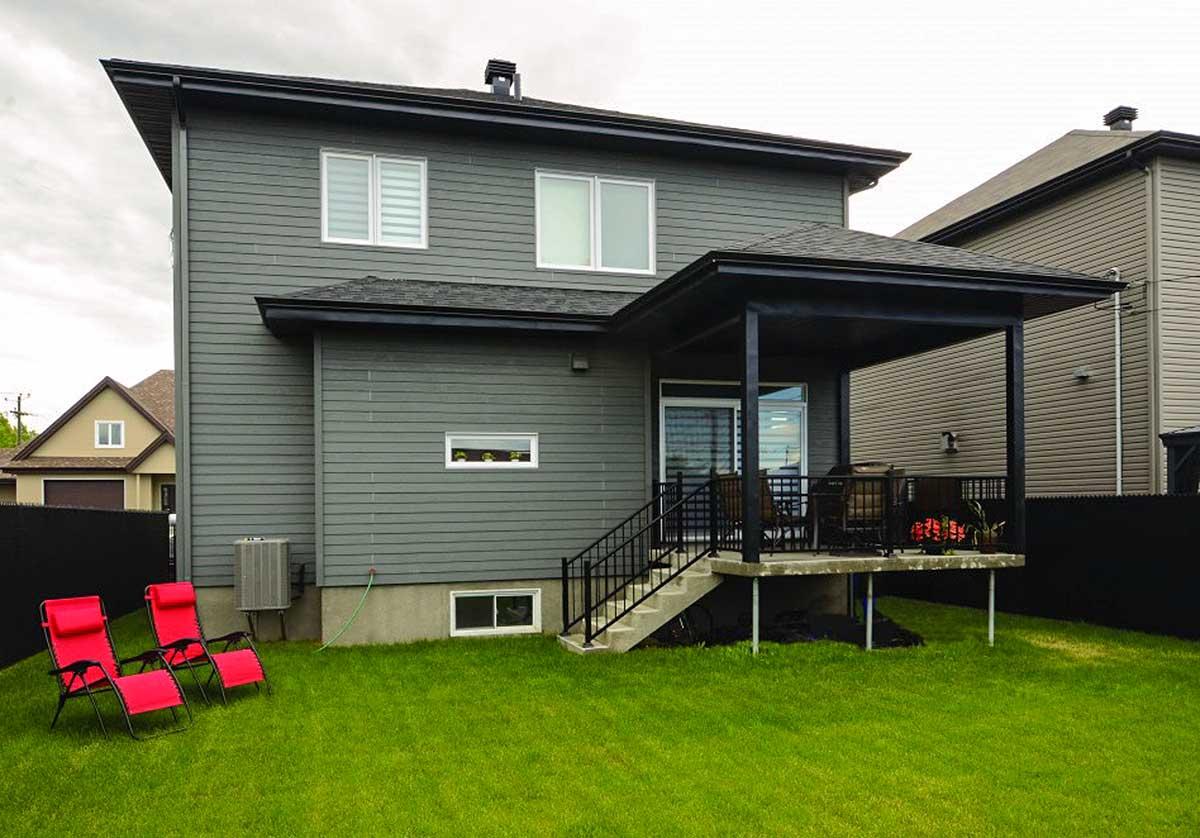 Two-story house exterior with horizontal siding, covered rear deck with stairs, and multiple windows.