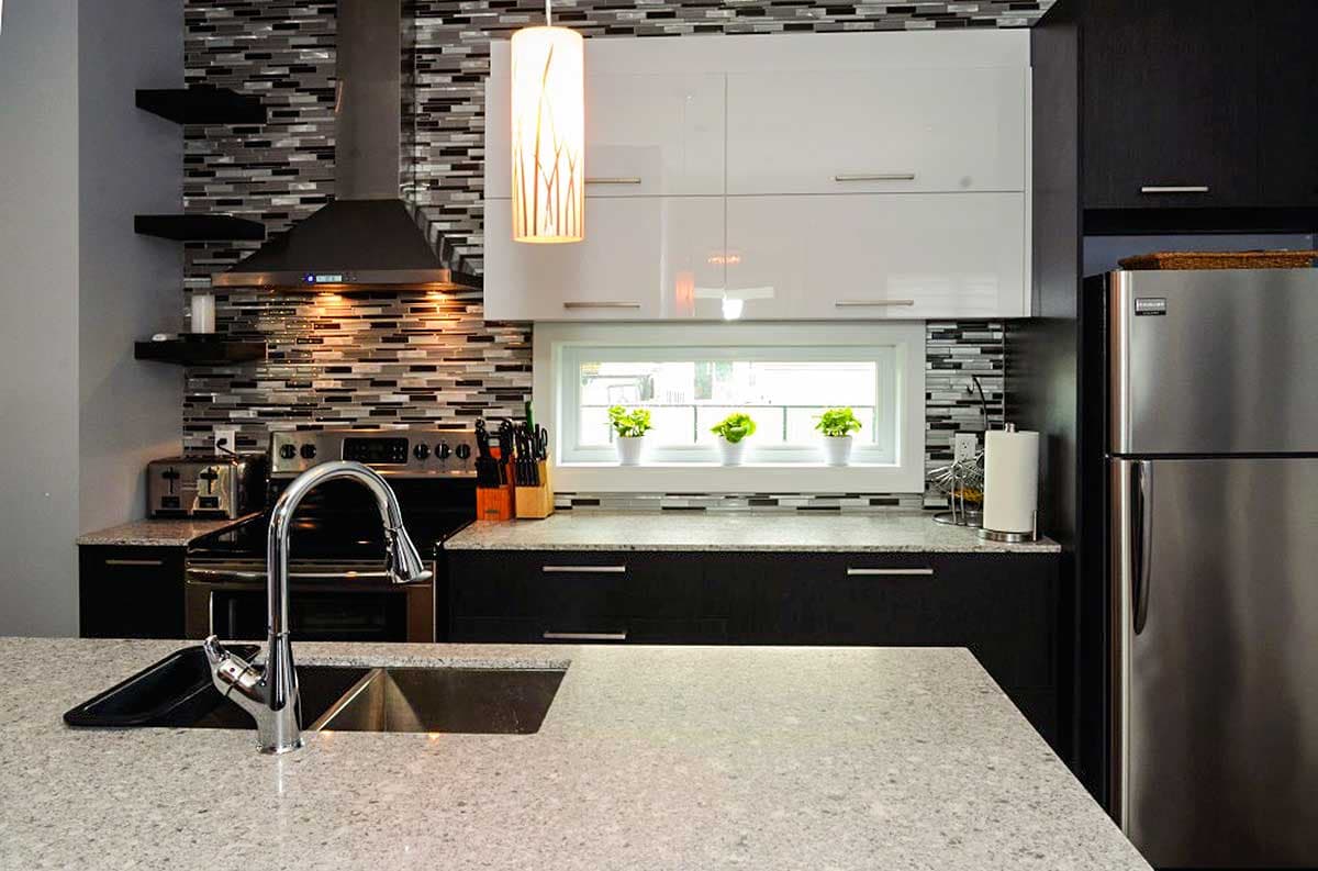 Modern kitchen with mosaic tile backsplash, stainless steel appliances, and white high-gloss cabinets above a horizontal window.