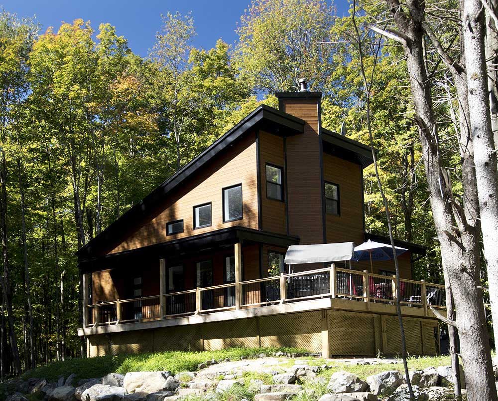 Modern two-story house plan exterior with wood siding, asymmetric rooflines, covered porch, and wraparound deck.