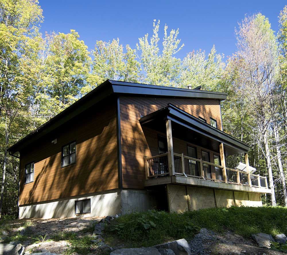 Modern house plan exterior with wood siding, concrete foundation, and a covered deck with railings.