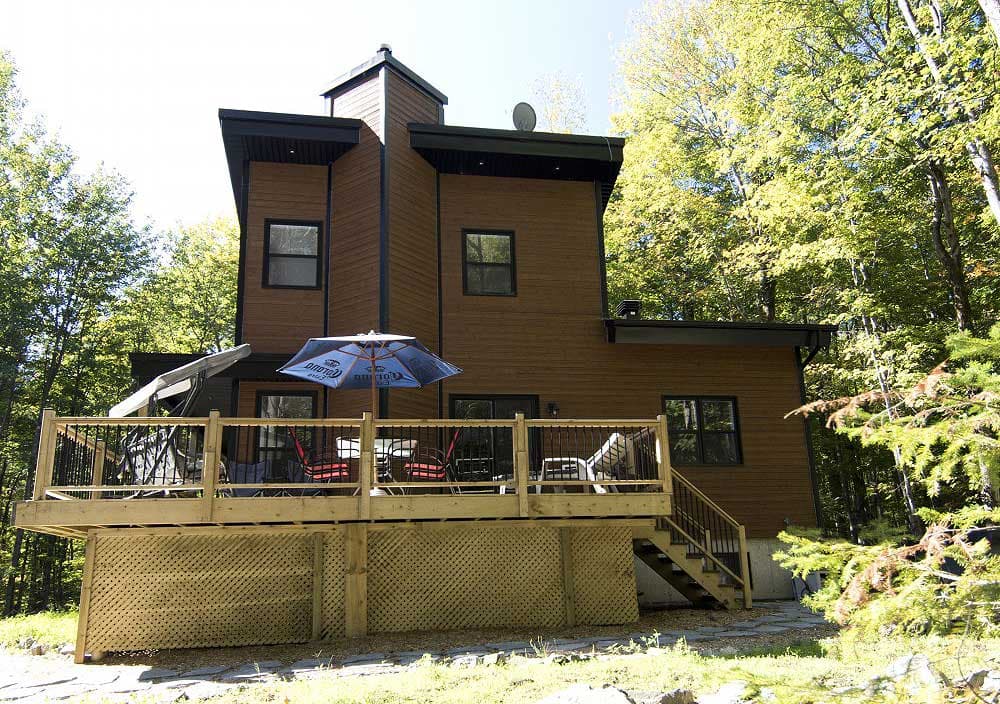 House plan exterior: Two-story modern home with wood siding, expansive deck, and prominent gable rooflines.