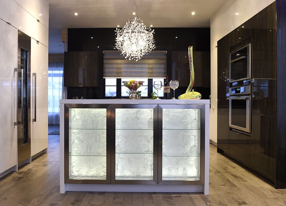 Modern kitchen with island featuring glass-fronted cabinets, stainless steel appliances, and contemporary lighting.