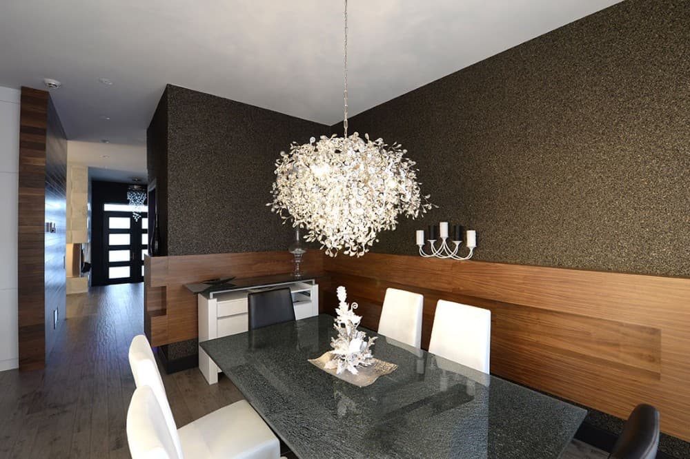 Dining room with granite table, modern chandelier, wood paneling, and view into entryway with frosted glass door.