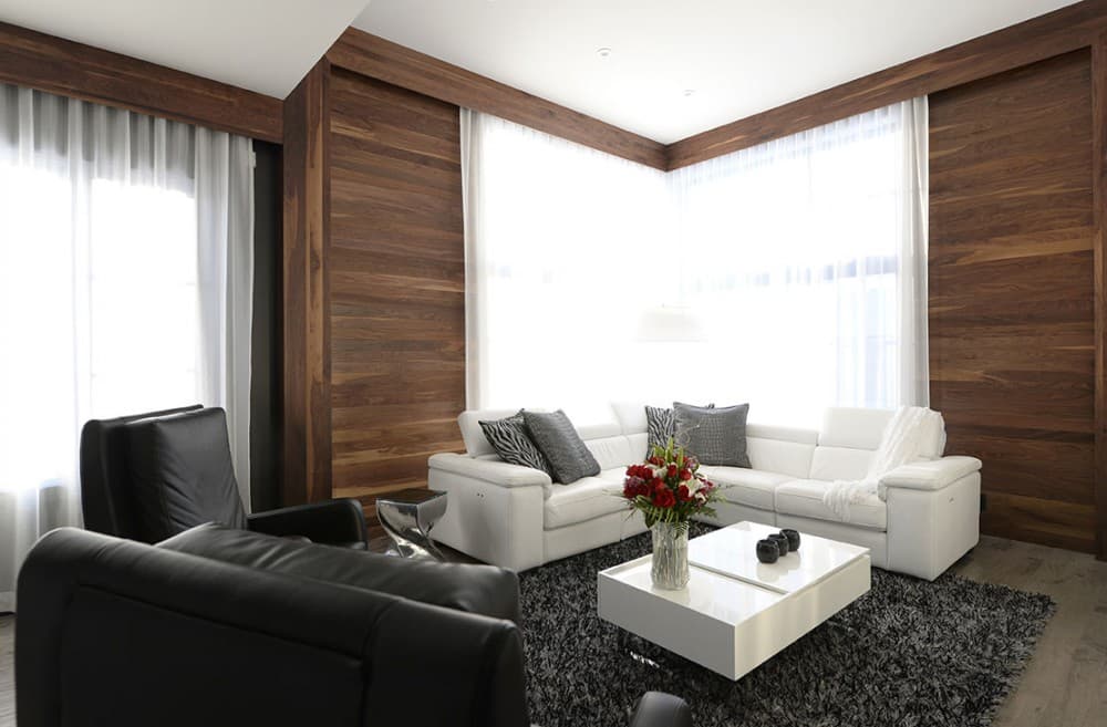 Living room with white sectional sofa, modern white coffee table, and dark wood paneled walls.