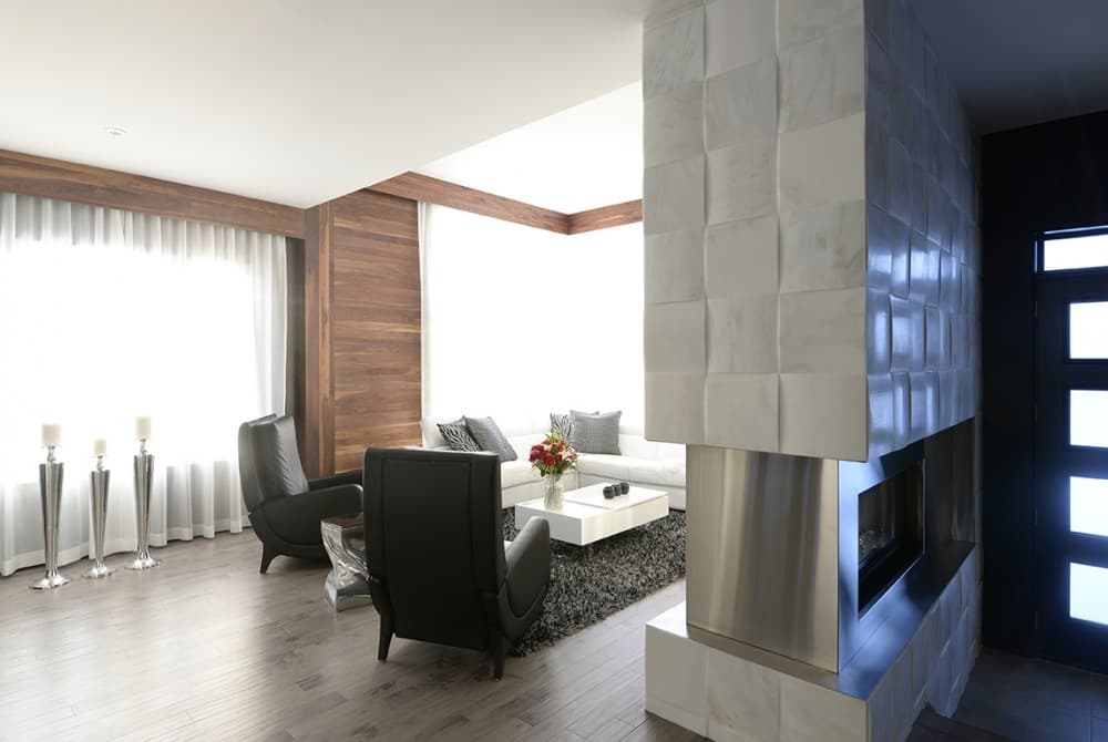 Interior view of a living room with a sectional sofa, modern fireplace, wood paneling, and large windows.