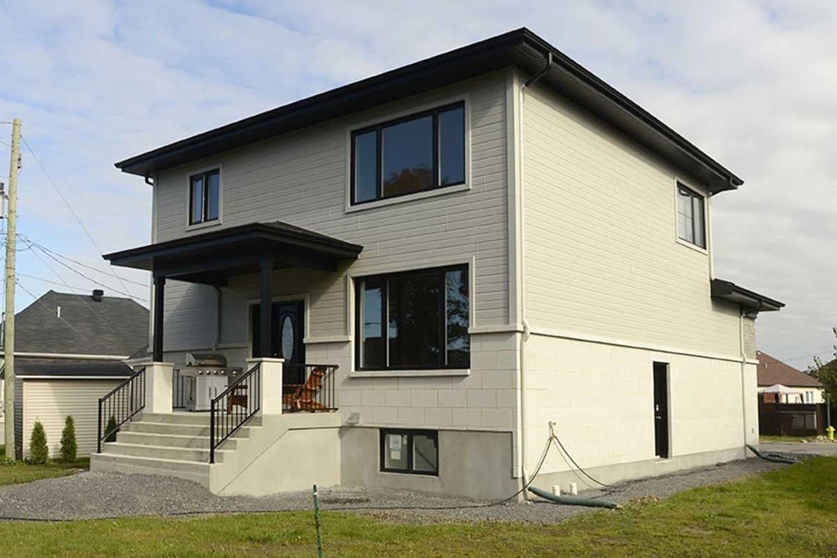 Two-story house plan exterior with covered front porch, large windows, and vinyl siding over block foundation.