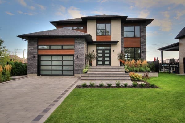 Modern two-story house plan exterior with stone and wood siding, glass garage door, and prominent entryway.