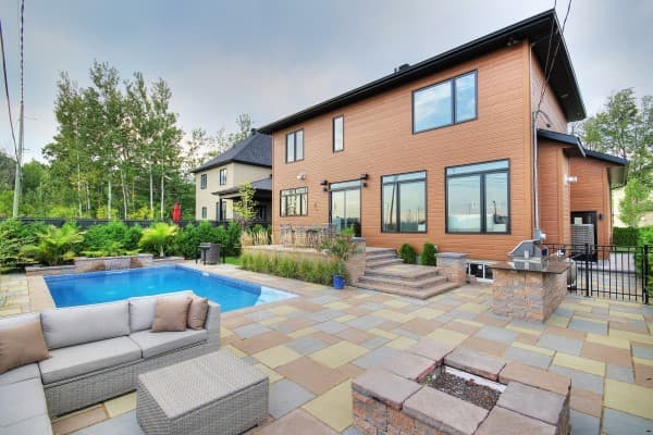Modern house exterior with a two-story design, featuring wood siding, large windows, an attached garage, and a backyard pool and patio area.