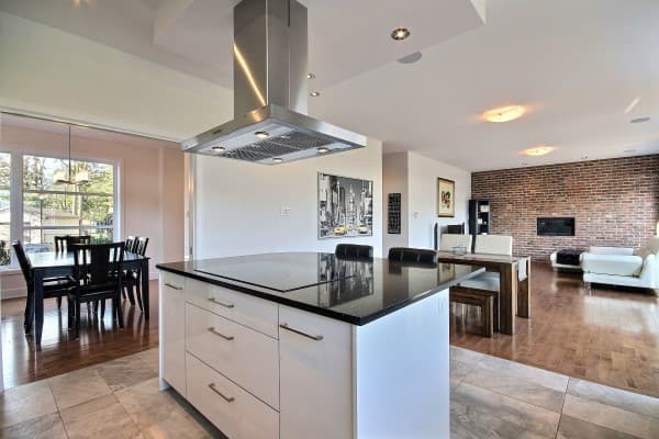 Open-concept kitchen with island and dining area, adjacent to living room with brick accent wall and fireplace.