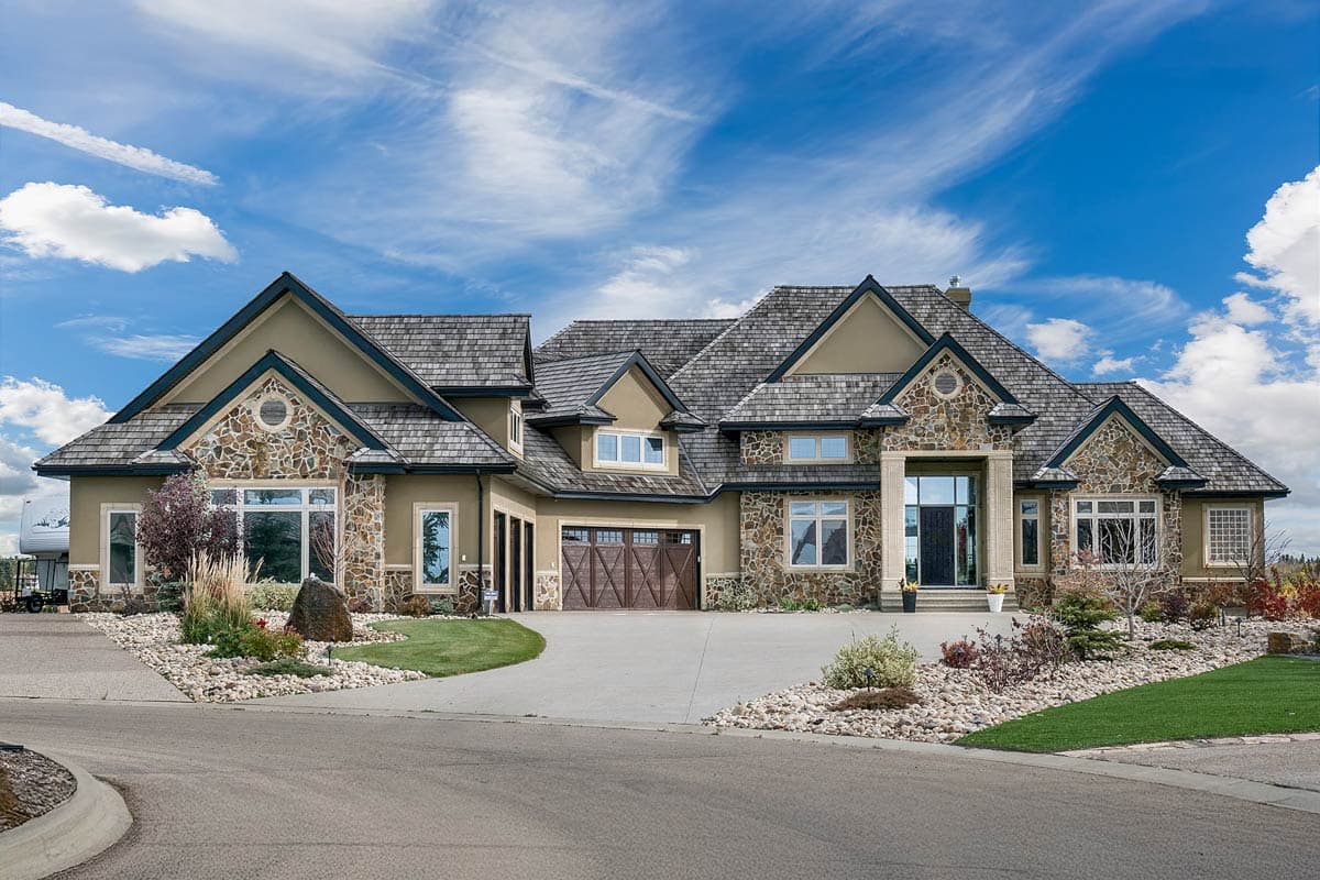 House plan exterior. Two-story home with stone accents, multiple gables, and a wood shake roof. Features include a three-car garage and large windows.