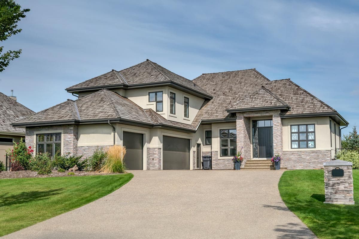 House plan exterior with a multi-level roof, stone accents, a two-car garage, and a covered entry with a dark door.