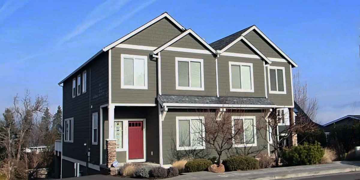 Two-story house plan exterior with stacked gables, horizontal siding, white trim, and a prominent red front door.