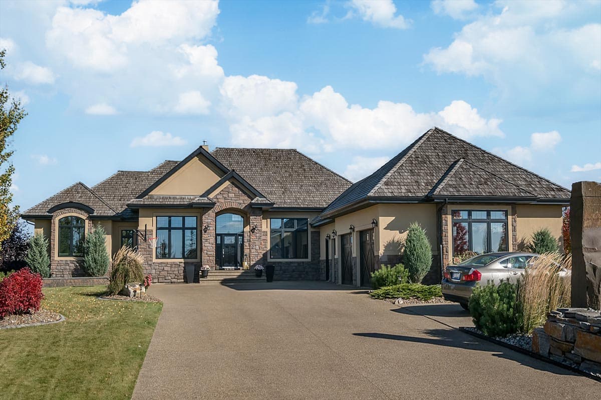House plan exterior of a one-story home with a stone and stucco facade, multiple gables, arched windows, and an attached three-car garage.
