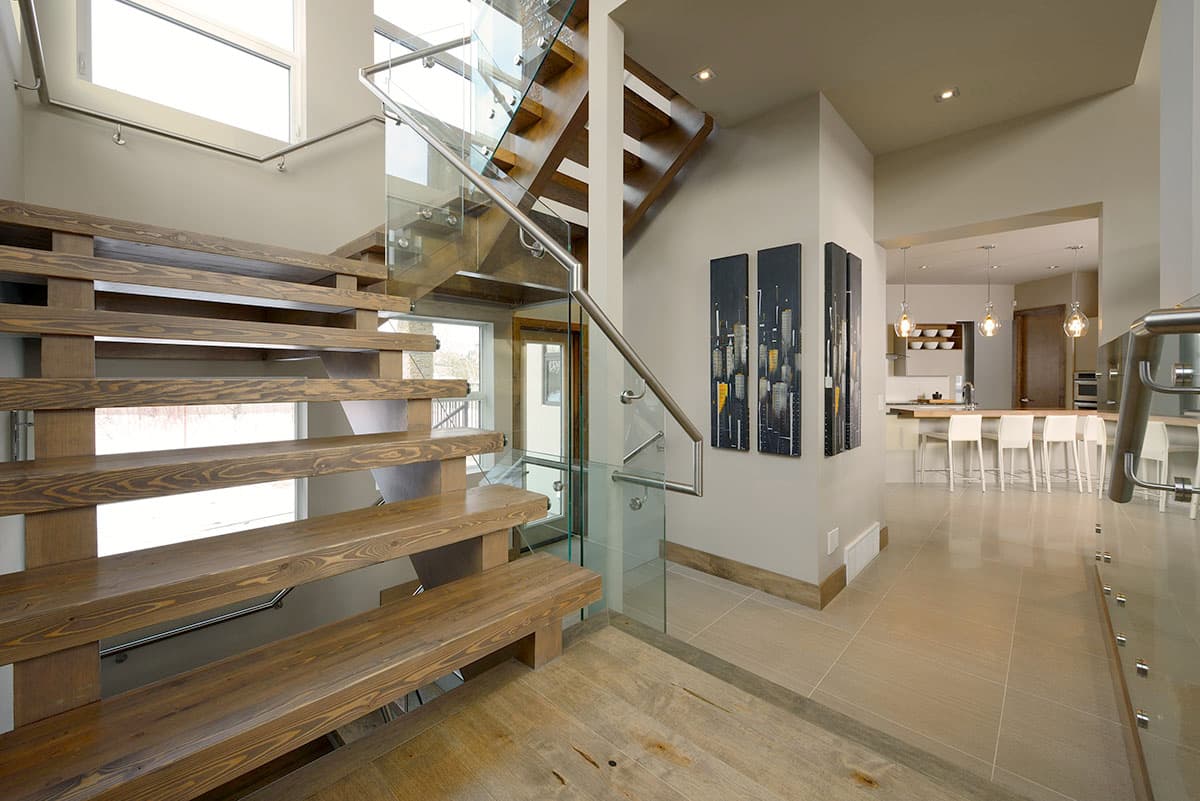 Modern open-concept interior featuring a floating wood staircase with glass railings and a view of the kitchen island with bar seating.