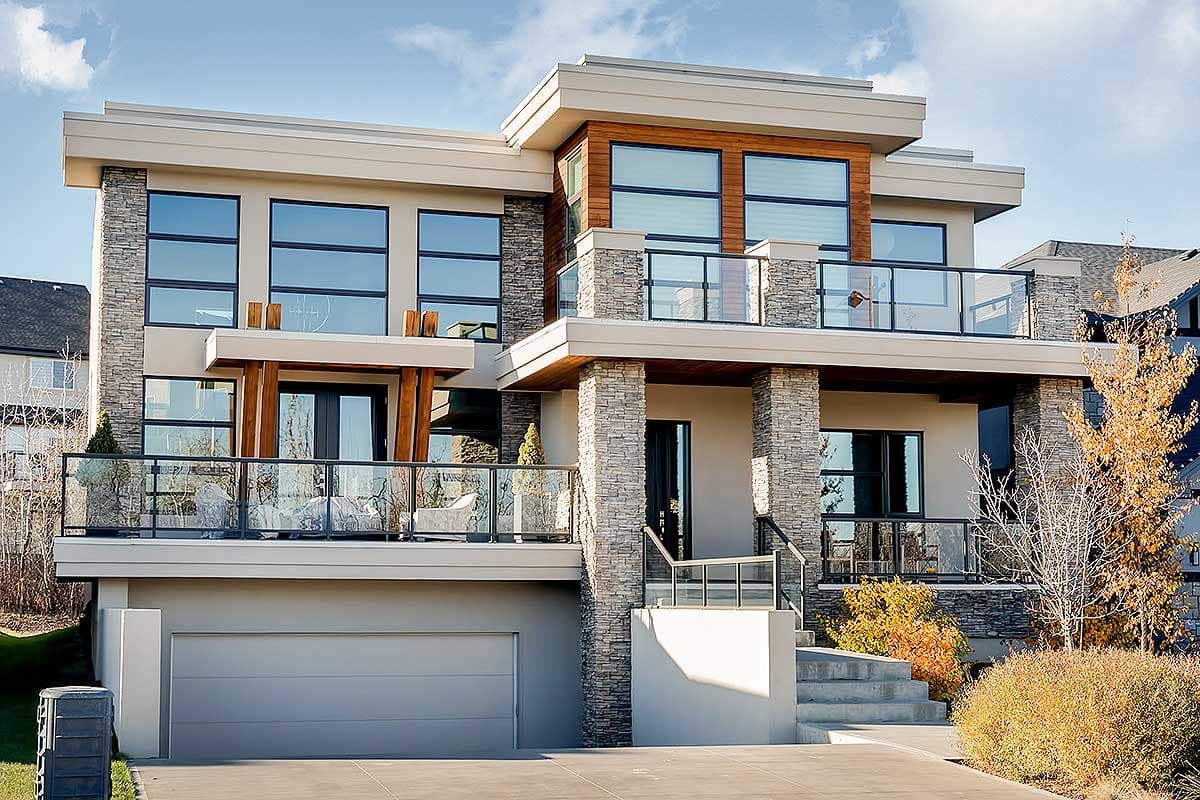 House plan exterior with modern design. Two-story home with stone accents, a cantilevered balcony, and a two-car garage.