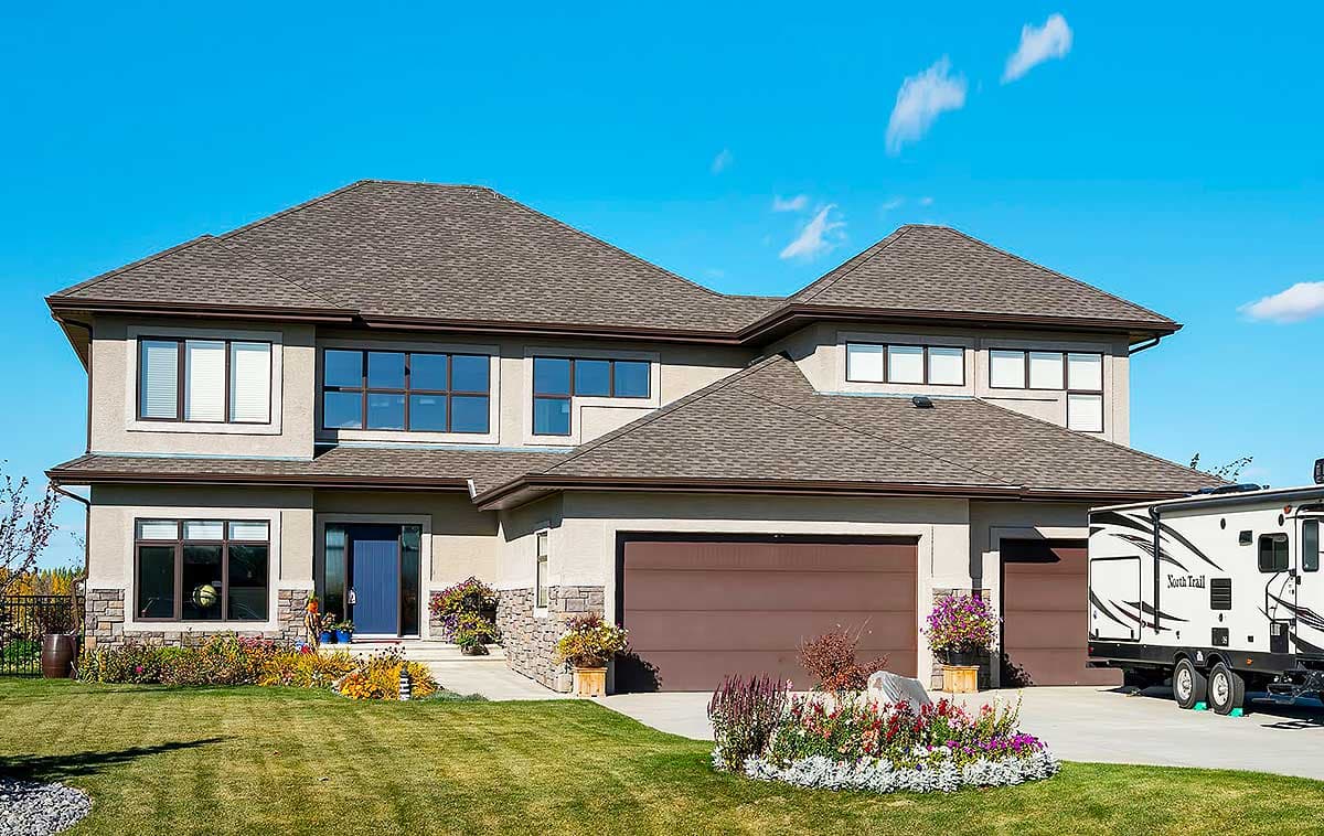 House plan exterior: Two-story home with attached two-car garage, prominent gables, stone accents, and large windows.