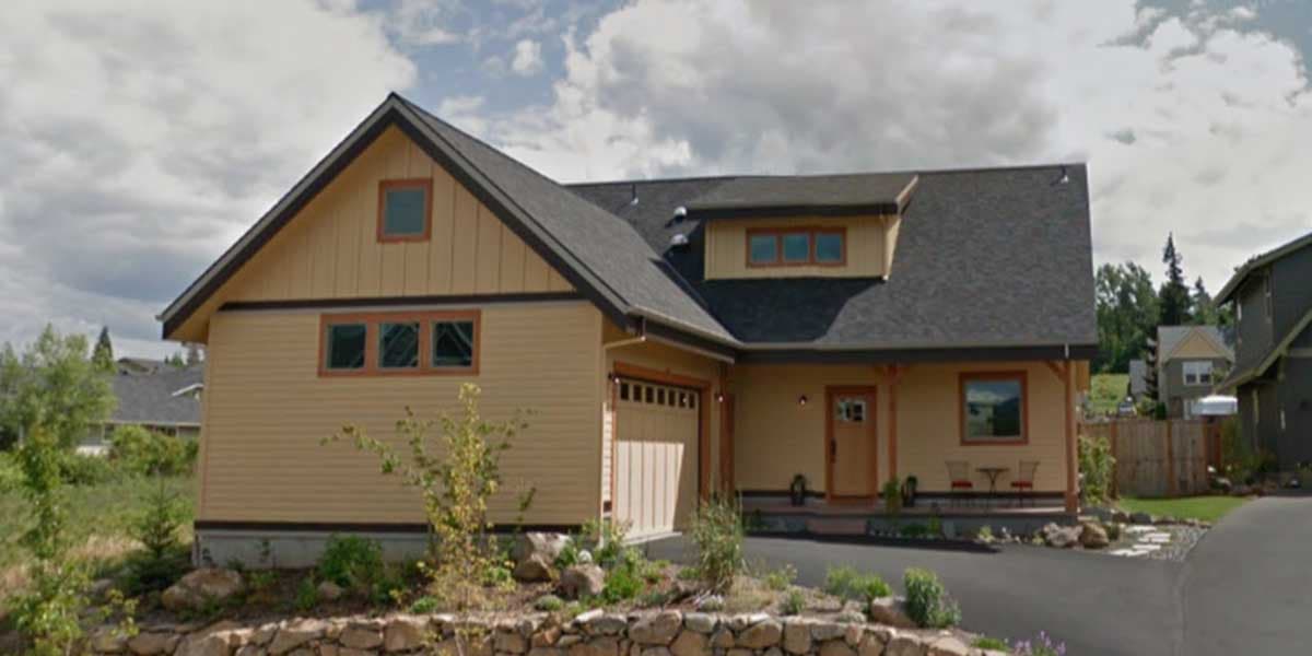 House plan exterior: tan siding, gabled roof, dormer, and attached garage with wooden door.