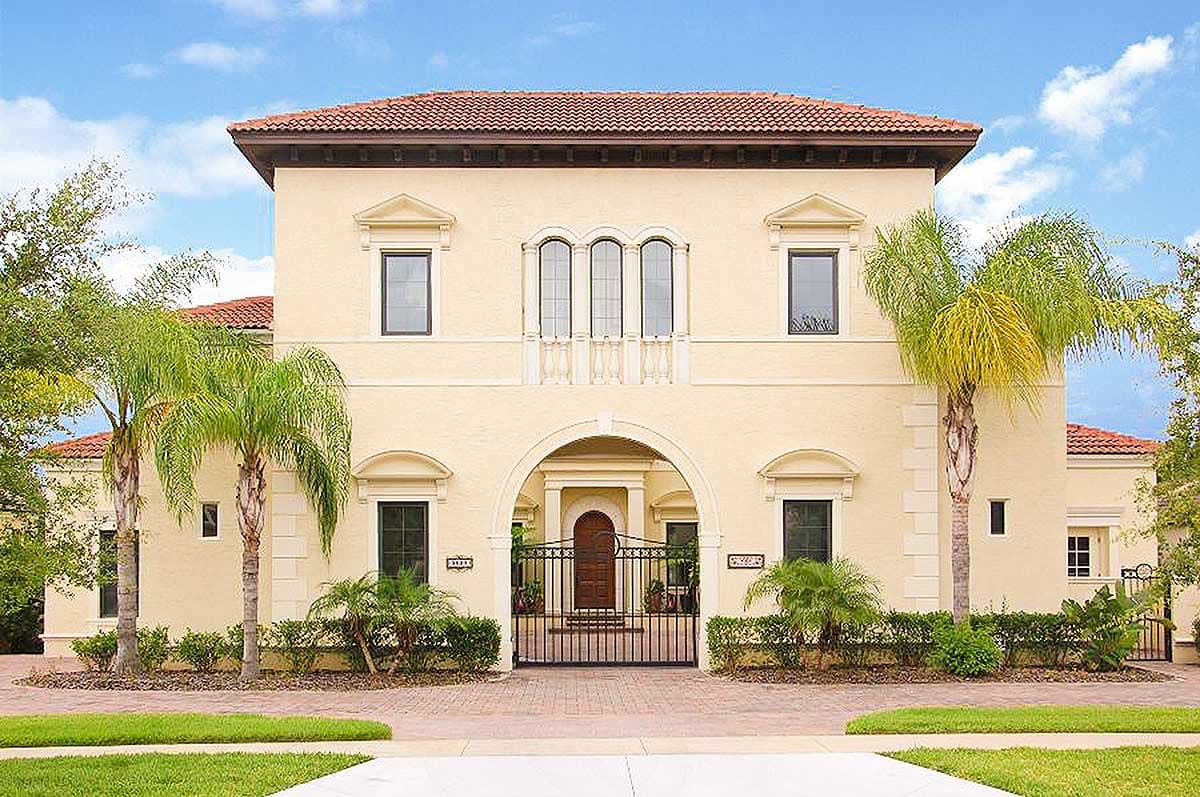 House plan exterior. Two-story Mediterranean style home with arched entry, terracotta tile roof, and wrought iron gate.