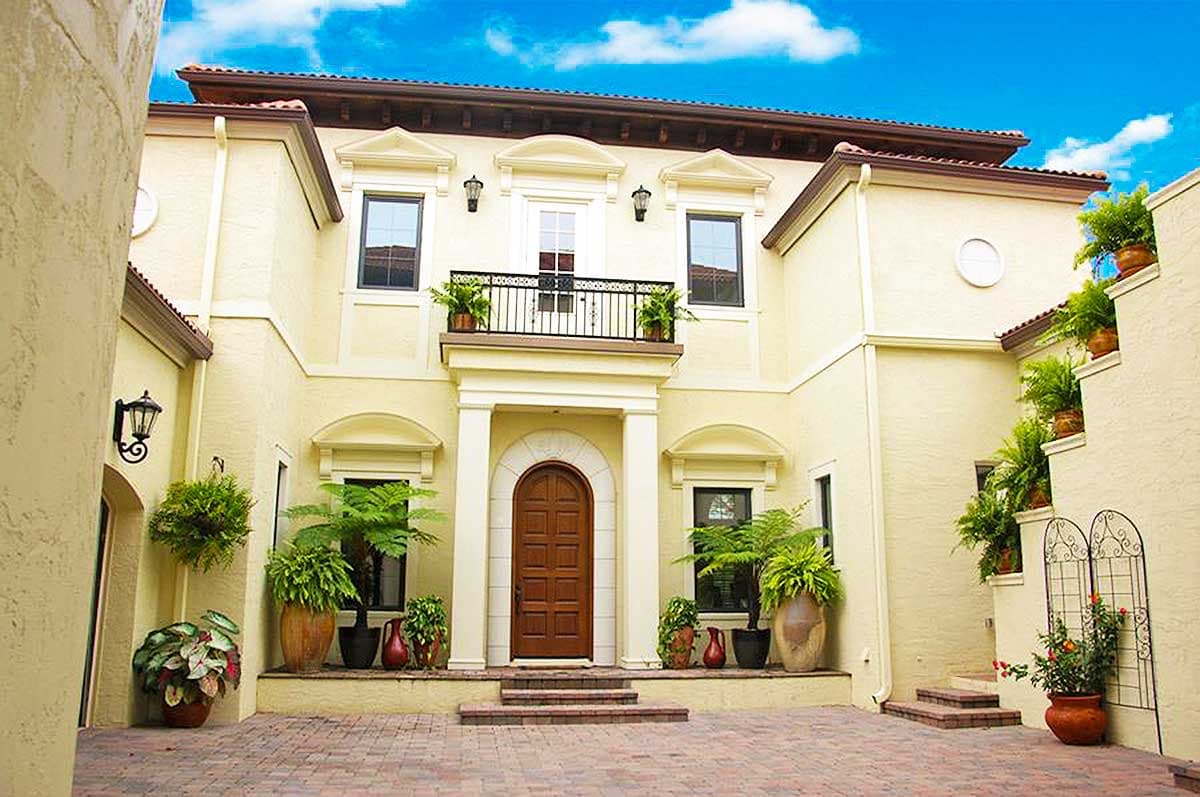 House plan exterior: Mediterranean style, two stories, arched entry, balcony with railing, stucco facade, tile roof.