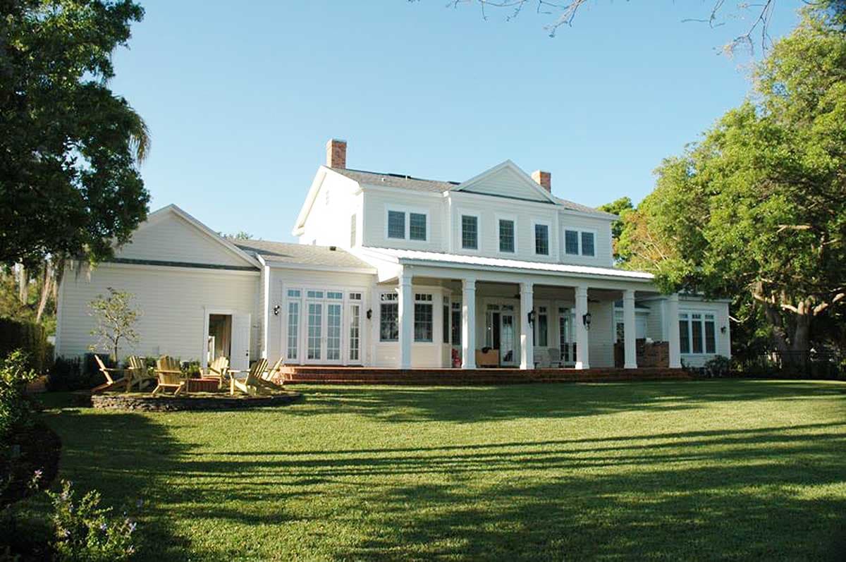 House plan exterior: Two-story white house with a wraparound porch, dual gables, and dormer windows.