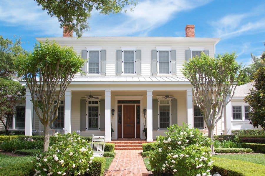 Two-story house plan exterior with a central gable, full-width covered porch supported by columns, and multiple windows with shutters.