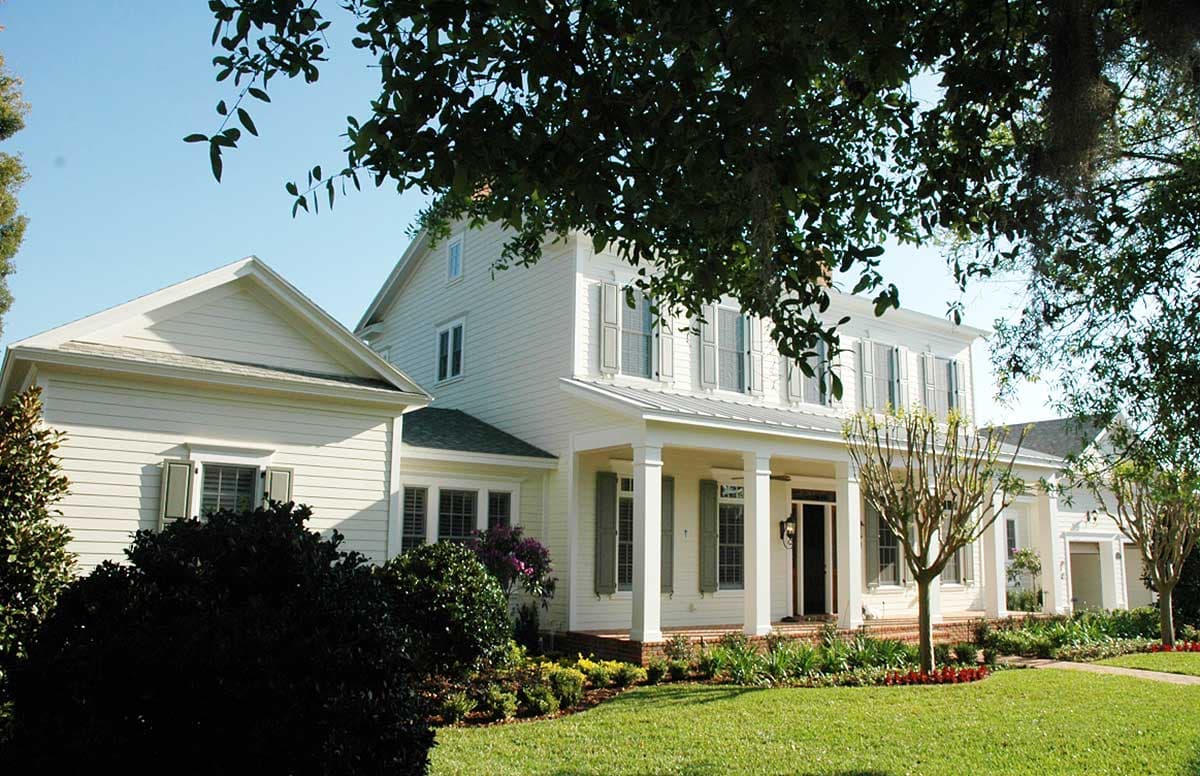 House plan exterior: two-story white house with a wraparound porch, gables, and a metal roof.