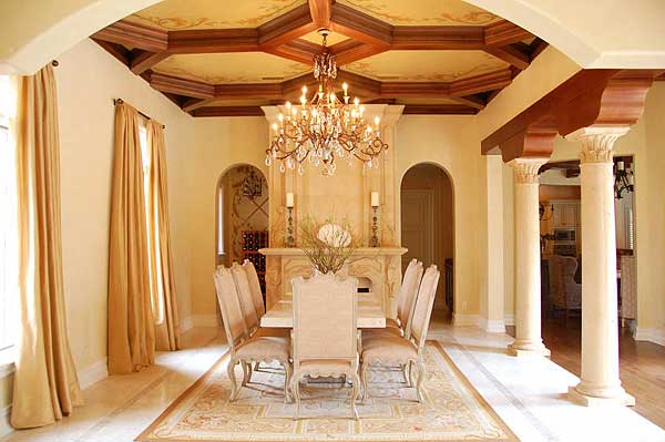 Dining room with coffered ceiling, fireplace, columns, and ornate chandelier.
