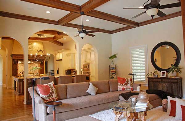 Interior view of a living room and kitchen with coffered ceilings, arched doorways, island seating, and a large sectional sofa.