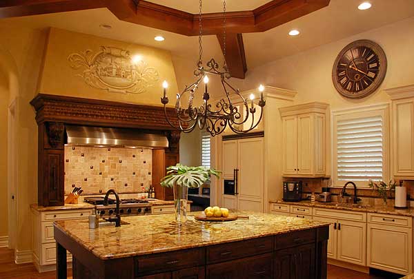 Kitchen interior with large island, ornate range hood, tile backsplash, cream cabinetry, and coffered ceiling.